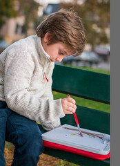 Portrait of a 7-year-old boy drawing in the park on an autumn day
