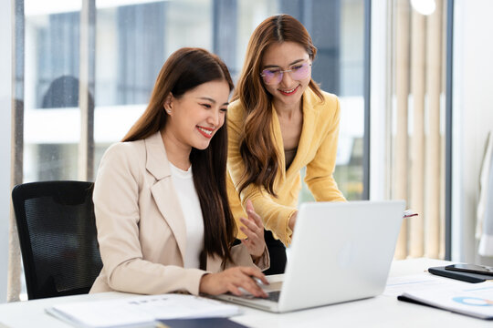 Young businesswomen sit at desk in office work together on laptop discuss ideas. female employees colleagues brainstorm on computer at meeting. Teamwork concept.