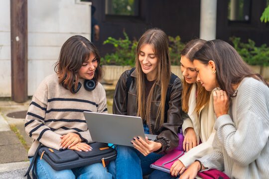 Young women friends studying together using laptop outdoors