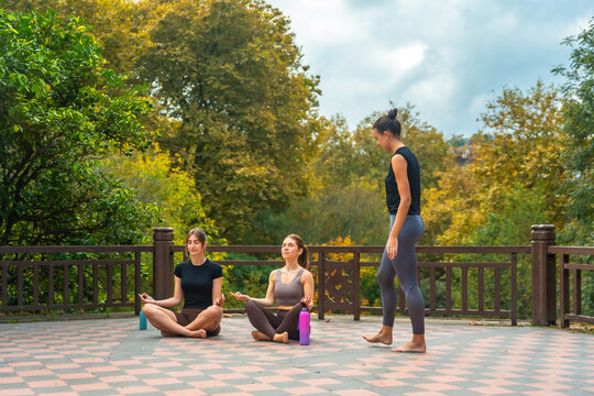 Women meditating in lotus pose with yoga instructor outdoors