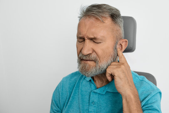 Elderly man experiences discomfort touching his ear, showing signs of hearing loss sitting in ENT clinic indoor