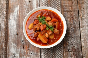 Delicious cooked stew in bowl on wooden table, top view