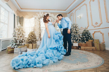 a young pregnant girl in a lush festive blue dress and a young man in a blue shirt. man kisses woman's hand. expecting a child. Christmas mood. married couple. family photo session. family photo
