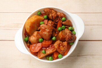 Delicious cooked stew in bowl on light wooden table, top view