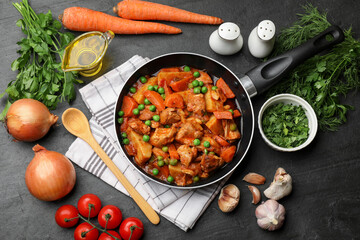 Delicious cooked stew in frying pan and ingredients on black table, flat lay