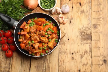 Delicious cooked stew in frying pan and ingredients on wooden table, flat lay. Space for text