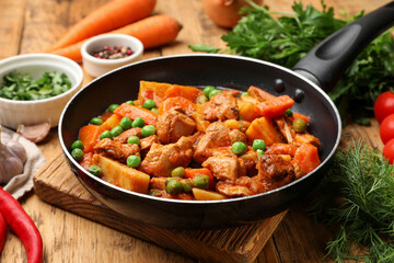 Delicious cooked stew in frying pan and ingredients on wooden table, closeup