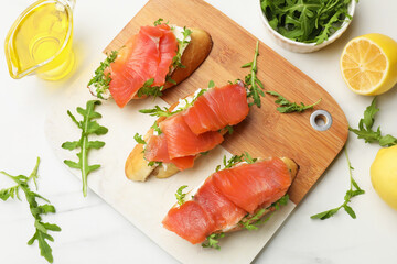 Tasty bruschettas with salmon and arugula served on white marble table, flat lay