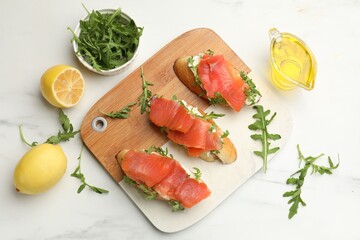 Tasty bruschettas with salmon and arugula served on white marble table, flat lay