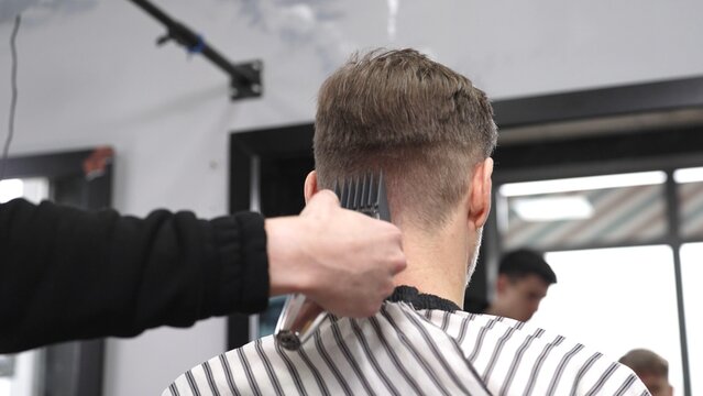 Professional hairstylist trimming client's hair using electric clippers, creating sleek, contemporary haircut with expert technique in modern barbershop setting