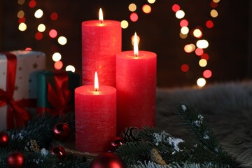 Burning candles, fir tree branches, cones, gift boxes and baubles on faux fur against black background with blurred lights, closeup with space for text. Christmas greeting card