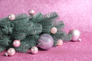 Beautiful fir tree branches with Christmas ornaments on shiny pink background, closeup
