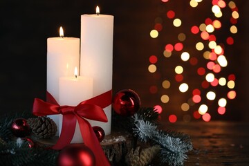 Burning candles, fir tree branches and baubles on wooden table against black background with...