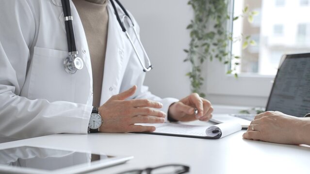 Doctor man is explaining diagnosis to female patient during a medical consultation in a medical office, gesturing with hands. Medicine and health care