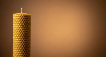 A beeswax candle with a honeycomb pattern sits against a warm brown background for a cozy natural vibe