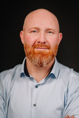 Confident man with a well-groomed beard and blue shirt poses against a dark background, showcasing a professional demeanor and engaging expression for portrait photography