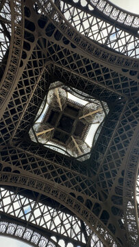 Extreme low-angle vertical shot capturing the dizzying, symmetrical, and abstract geometric patterns of the iconic Eiffel Tower's iron framework.
