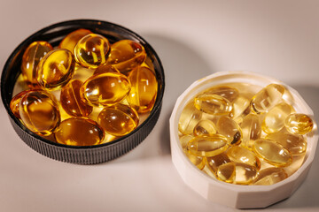 A close-up of golden translucent  capsules, housed in white and black plastic lids, in warm lighting to emphasize their shine and clarity.