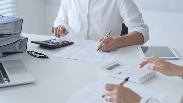 Two accountants collaborating in a well lit office, analyzing financial data and preparing reports with calculators and pens. Audit and taxes in business - Powered by Adobe