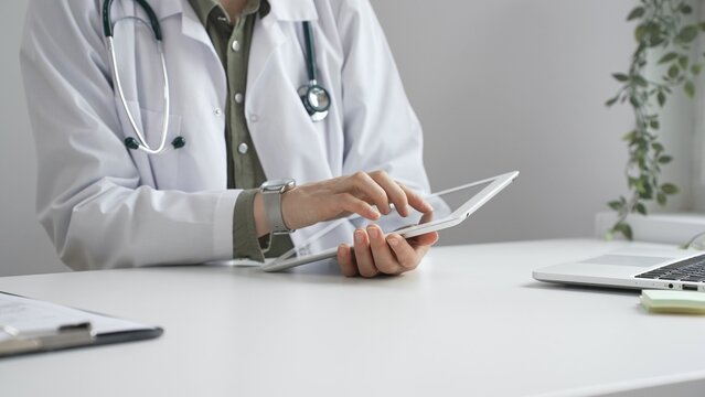Doctor woman in lab coat and stethoscope using digital tablet at desk in medical office, accessing online patient information. Medicine and health care concept - Powered by Adobe