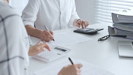 Professional accountants collaborating in a well lit office, analyzing financial data and preparing reports with calculators and pens. Audit and taxes