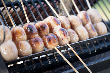 Grilled sausage skewer street vendor grill Thai snack food smoky charcoal heat rustic metal rack outdoor market thailand savory pork filling juicy brown crust