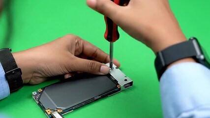 Close up view of hands carefully repairing a smartphone using a screwdriver against a solid green backdrop highlighting technology repair services and sustainable