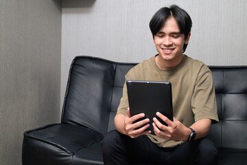 Portrait of handsome Young Asian Thai man using digital tablet computer at home