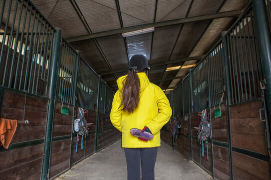 Child girl holds brush at horse stable corridor