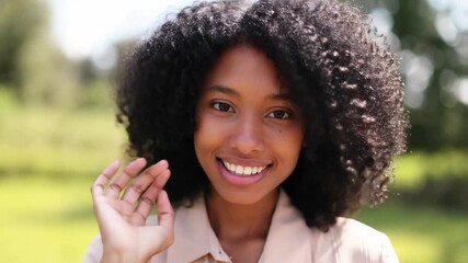 A beautiful woman with curly hair waves hello with a warm smile and welcoming gesture. Her eyes are bright and full of life Stock Video