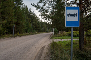 A bus stop sign on a country road in the woods.Laying a bus route to hard-to-reach places.