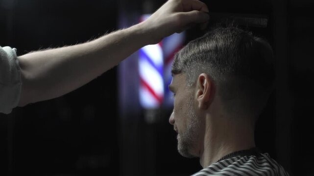 Professional barber carefully checking customer's hair texture and head contours, preparing for precise haircut, vintage barbershop interior with iconic striped pole visible
