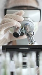 Close up of white gloved hand of a scientist adjusting a microscope in a laboratory. Medicine, health care and science concept
