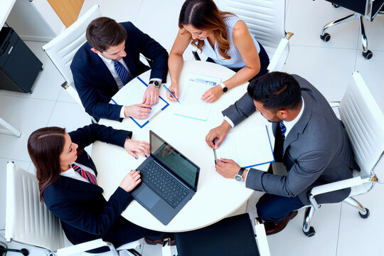 Group of young adult multiethnic business professionals collaborating around table, discussing documents and using laptop during meeting, top view showing teamwork and cooperation