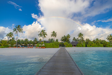 Fantastic view over wooden pier turquoise calm ocean shore sand beach palm trees sunny blue sky and rainbow. Tropical island resort landscape. Perfect summer holiday travel destination tourism scenic