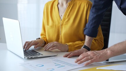 Business colleagues collaborating on a project while analyzing financial charts and entering data on a laptop in a modern office. Businesspeople concept