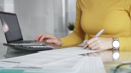 Woman calculating budget and reviewing financial documents using a laptop and calculator for home finances. Audit and taxes in business - Powered by Adobe