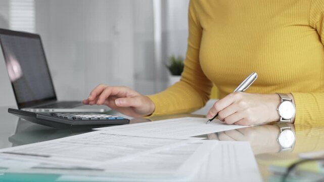 Woman calculating budget and reviewing financial documents using a laptop and calculator for home finances. Audit and taxes in business