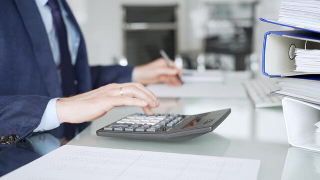 Accountant working in office, calculating finance data using black calculator and taking notes for budget planning. Audit and taxes in business - Powered by Adobe