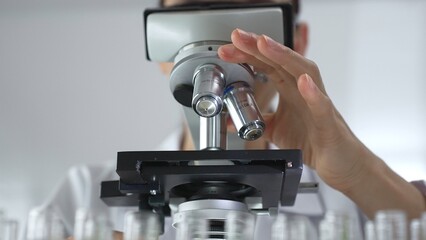 Female scientist analyzing test samples under microscope in contemporary research environment of laboratory. Medicine, healthcare and science concept