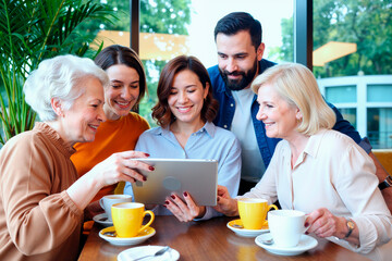 Group of multiethnic adults and seniors gathering around table, smiling and interacting while using digital tablet, sharing information and enjoying conversation in modern cafe setting