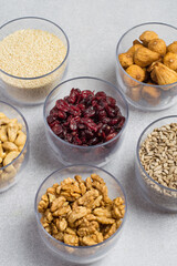 An assortment of nuts, dried fruits, and seeds in transparent containers on a light gray background. Healthy products, natural food. Food storage.
