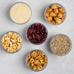 An assortment of nuts, dried fruits, and seeds in transparent containers on a light gray background. Healthy products, natural food. Food storage.