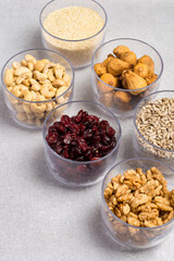 An assortment of nuts, dried fruits, and seeds in transparent containers on a light gray background. Healthy products, natural food. Food storage.