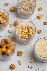An assortment of nuts, dried fruits, and seeds in transparent containers on a light gray background. Healthy products, natural food. Food storage.