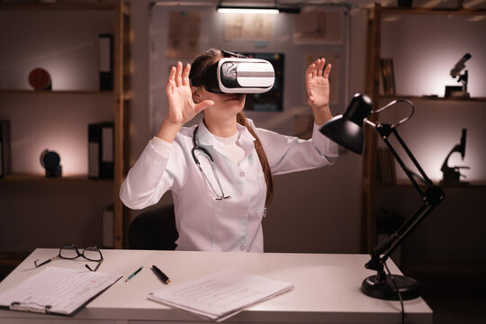 woman doctor using VR virtual reality goggles to medical exam working on night shift in medical office hospital