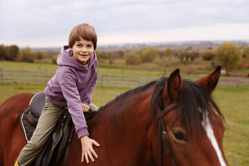 Obraz premium Equine assisted therapy. Little boy stroking horse while riding outdoors. Lovely domesticated pet