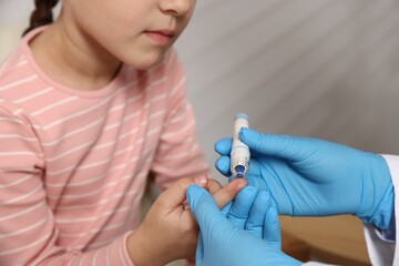 Diabetes. Doctor in medical gloves checking little girl's blood sugar level with lancet pen...