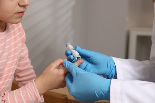 Diabetes. Doctor in medical gloves checking little girl's blood sugar level with lancet pen indoors, closeup