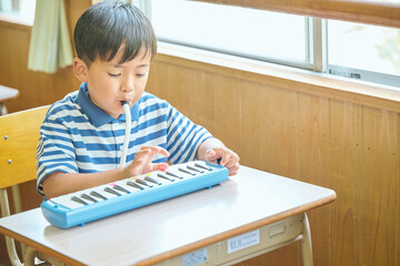 Naklejka premium 教室で鍵盤ハーモニカを演奏する小学生の男の子
